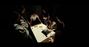 Frame from Heirloom: people gathered around a lit table in the dark, seen from above