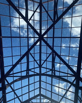 A glazed roof structure against a blue sky with clouds