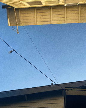 The corner of a roof against a clear sky crossed by wires